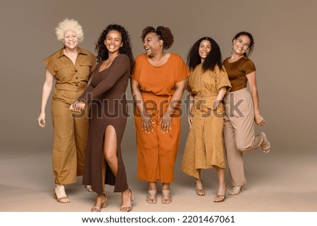 Full length studio portrait of a group of beautiful multiracial women laughing with each other on a neutral background.