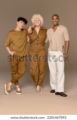Full length shot of a non-binary Caucasian person in their 20's, a Black woman with albinism in her 20's, and a Hispanic man in his 20's smiling together on a neutral background. Royalty-Free Stock Photo #2201467093