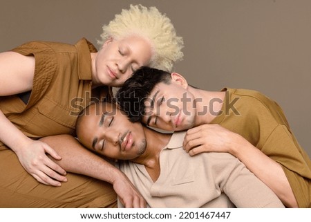 Portrait of a non-binary caucasian person in their 20's, a Black woman with albinism in her 20's, and a Hispanic man in his 20's leaning against each other with their eyes closed. Royalty-Free Stock Photo #2201467447