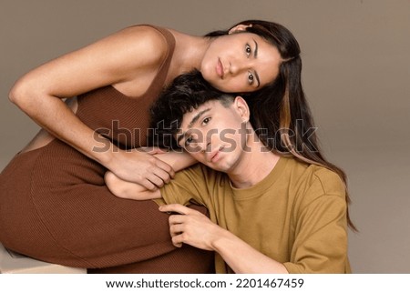 Portrait of a Puerto Rican woman in her 30's and a non-binary caucasian person in their 20's leaning against each other on a neutral background. Royalty-Free Stock Photo #2201467459