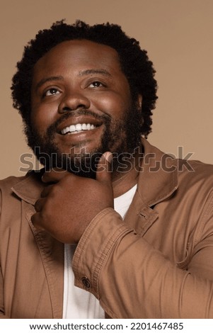 portrait of african american man in his 30s smiling confidently and posing with hand on chin on neutral background