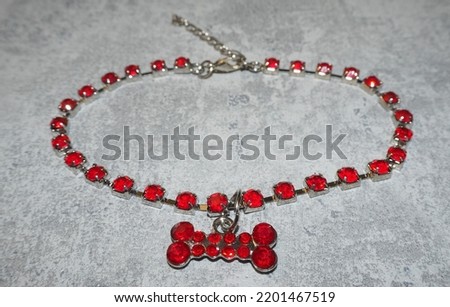 a metal necklace with red stones and a dog bone pendant lies on a gray background.  side view.  small dog collar
