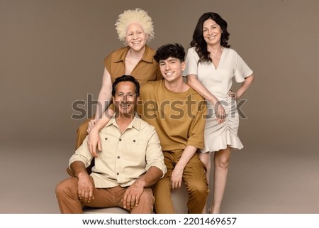 Studio shot of a Black woman with albinism in her 20's, a Hispanic woman in her 50's, a non-binary caucasian person in their 20's, and an Indian man in his 50's smiling at the camera. Royalty-Free Stock Photo #2201469657