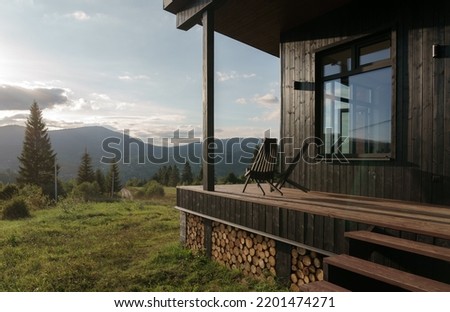 Black wooden chairs on cabin terrace with mountain view at sunset