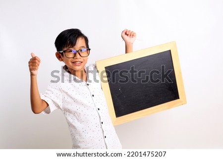 Happy asian schoolboy standing while showing a blank blackboard and thumbs up. Isolated on white