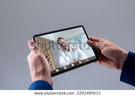 Hands of caucasian man making tablet video call with caucasian male doctor. Medical services, telemedicine and digital interface concept.
