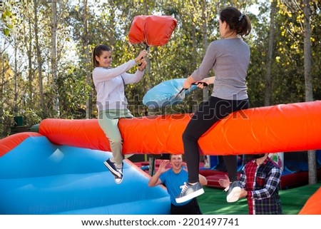 Female friends having funny wrestling by pillows on inflatable beam in outdoor amusement park