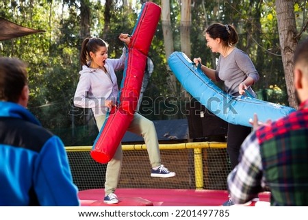 Happy female friends fighting by inflatable logs on adults bouncy playground outdoor