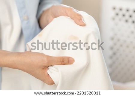 Housewife, asian young woman hand in holding shirt, showing making stain, spot dirty or smudge on clothes, dirt stains for cleaning before washing, making household working at home. Laundry and maid. Royalty-Free Stock Photo #2201520011