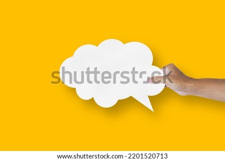 hand holding white paper cloud shape speech bubble balloon isolated on yellow background communication bubbles.
