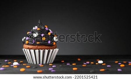 Cupcake on Halloween. Dessert on Halloween party. Muffin decorated with colored sprinkles, black frosting, icing. Cupcake on dark background. Macro high quality and resolution photo. Copy space