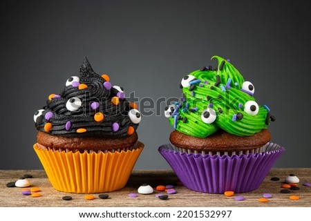 Cupcake on Halloween. Dessert on Halloween party. Chocolate muffin decorated with colored sprinkles, black, green frosting, icing. Cupcakes on dark background and wooden desk. Macro high quality photo