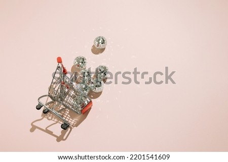 Overturned shopping cart with disco balls falling out on pink background.