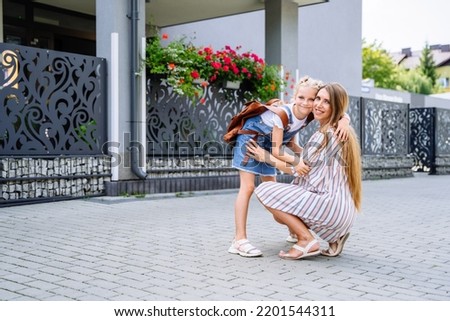 Pregnant mother hugging little daughter schoolgirl with brown backpack, saying goodbye before first day in school, standing together outdoor, loving mom leading child to second grade. Royalty-Free Stock Photo #2201544311