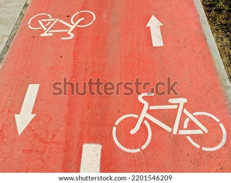 On the red bike path are white signs for the movement of bicycles in different directions.