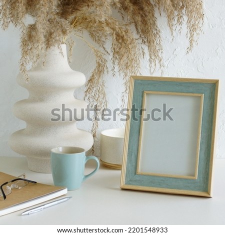 Modern women's home office workspace with photo frame mockup.  Aesthetic scandy hygge style.Cup coffee, photo frame,planner, vase with grass,aroma candle .Copy space.Neutral colors home design. Royalty-Free Stock Photo #2201548933