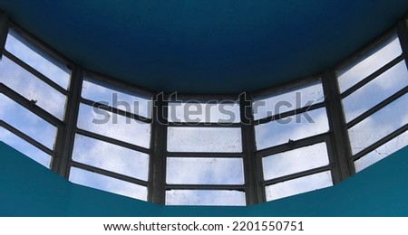 Five angled windows form part of a skylight in an old building. A blue sky contrasts against the black frames and the old dirty glass