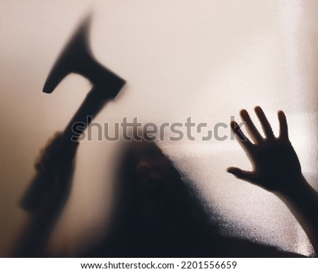 Horror, halloween background - Shadowy figure behind glass holding an axe