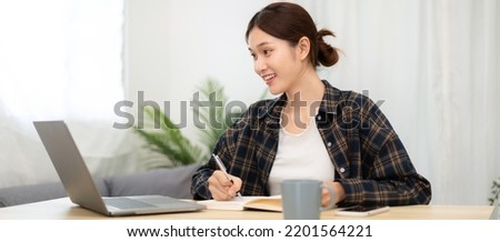 Teenage girl is listening lecture of lecturer and taking notes on notebook while using laptop to studying e-learning from study remotely at home.