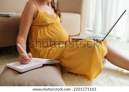 Pregnant woman watching videos on childbirth and childcare and writing ideas in planner Royalty-Free Stock Photo #2201571163
