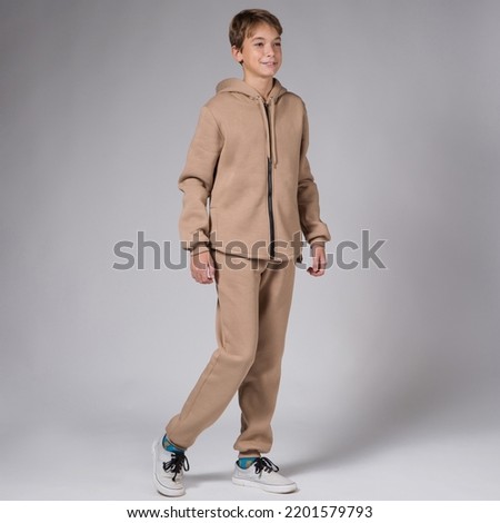 Boy teenager in a brown hoodie and sports pants, posing on a gray background, taking a step forward, studio photography