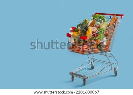 Shopping cart full of groceries on light blue background. Space for text Royalty-Free Stock Photo #2201600067