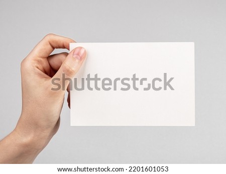 Hand holding card mockup on grey background. Empty space for congratulation, invitation, note. Paper in horizontal position. High quality photo Royalty-Free Stock Photo #2201601053