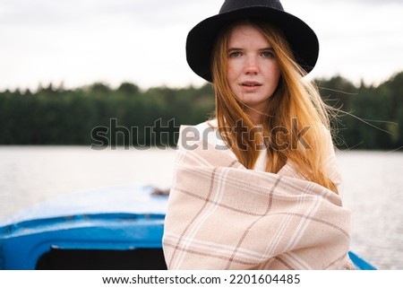 A girl in a sweater sails in a boat on an autumn day. Portrait of a beautiful redheaded woman on a lake.