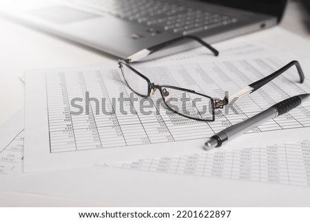 Invoices, accounting documents, pen, laptop and eyeglasses at the workplace in the office. Balance, budget, business and finance concept. Close-up, low angle view, selective focus. Royalty-Free Stock Photo #2201622897