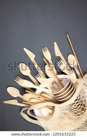 A set of disposable wooden tableware in a string bag on a gray background. Flat lay.