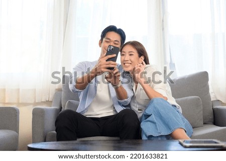 A Young smiling asian couple holding smartphone and making video call at home 