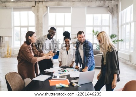 Multiracial male and female architects gathering at table with papers and gadgets while sharing ideas about new startup business plan Royalty-Free Stock Photo #2201646235