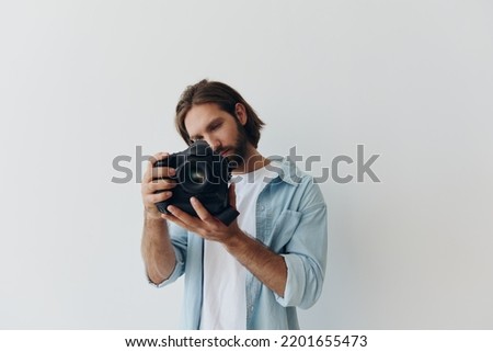 Man hipster photographer in a studio against a white background holding a professional camera and setting it up before shooting. Lifestyle work as a freelance photographer