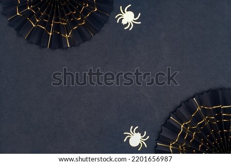 Golden spider and cobweb on a dark background with copy space. Scary Halloween shiny spiders and black paper fans with golden cobwebs. Halloween decorations on a black textured backdrop. Royalty-Free Stock Photo #2201656987