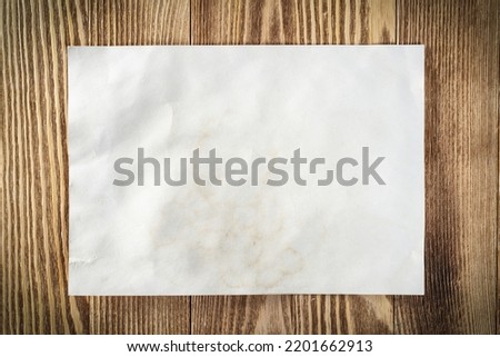 Flat lay wooden table with paper sheet. Blank white a4 format paper. Space for writing and notification. Textured natural wooden background for message. Vintage copy space for creative design.