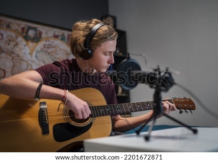 Home sound studio young teenager portrait playing guitar in Headphones and recording music using microphone. Modern audio recording technology concept image.