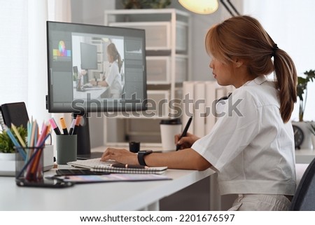 Young creative woman sitting at graphic studio in front of professional computer and editing photo