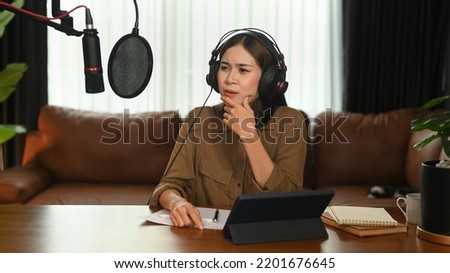 Concentrated female radio host listening to interesting conversation with guest during recording podcast in home studio
