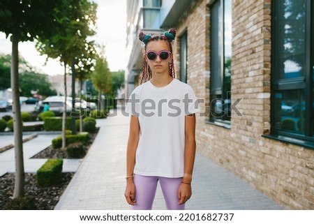 Portrait of a cute teenage girl with African braids in a white t-shirt and sunglasses stands on a city street. Mock-up for print. T-shirt template.