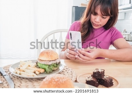 Asian woman taking pictures of hamburgers and chocolate brownies by her smartphone.