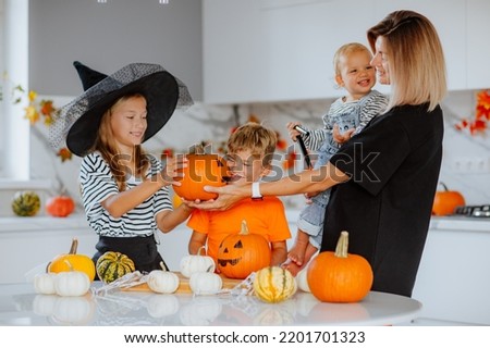 Happy mom with three young kids in halloween costumes are drawing pumpkins for a holiday on white kitchen. Happiness. Focus is at the middle pumpkin.