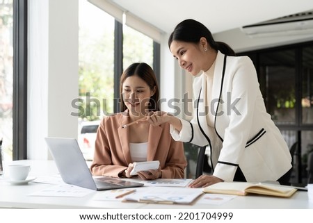 Young businesswoman adviser standing in front of laptop and giving advise to sales woman. Business people consulting at office. Royalty-Free Stock Photo #2201704999