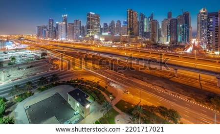 Dubai Marina skyscrapers and Sheikh Zayed road with metro railway aerial day to night transition panoramic timelapse. Traffic on a highway near modern towers after sunset, United Arab Emirates