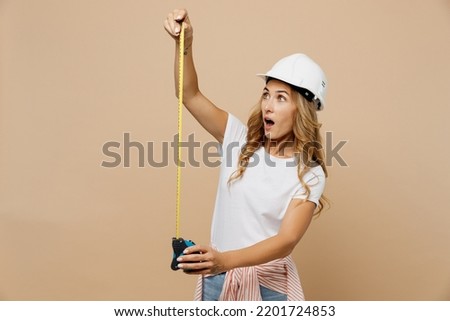 Young shocked surprised employee laborer handyman woman wear white t-shirt helmet use tape-measure isolated on plain beige background Instruments accessories for renovation room. Repair home concept