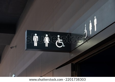 A sign of restroom lighten in white standout from a black plate. The restroom is inside a building, decorated in black and white tone.