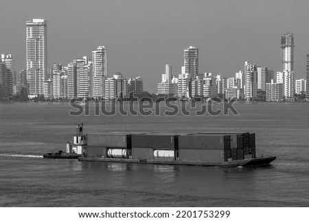 A cargo container on a calm sea against high-rise buildings, grayscale shot