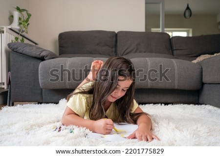 Cheerful little girl lying on the floor drawing . High quality photography