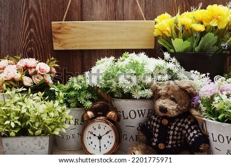 Empty wooden sign hanging with teddy bear and alarm clock on wooden background