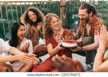 A girl celebrates her birthday at the rooftop party with friends. A girl blew out the candles and wished birthday wish. Friends are clapping and smiling.