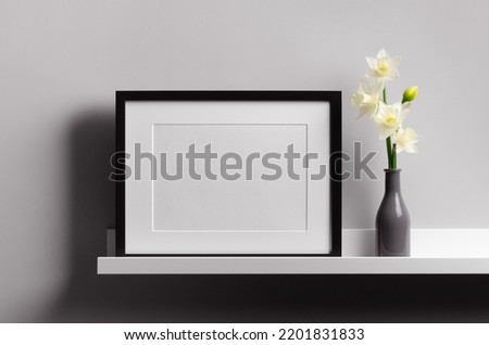 Landscape black picture frame mockup on shelf with flowers